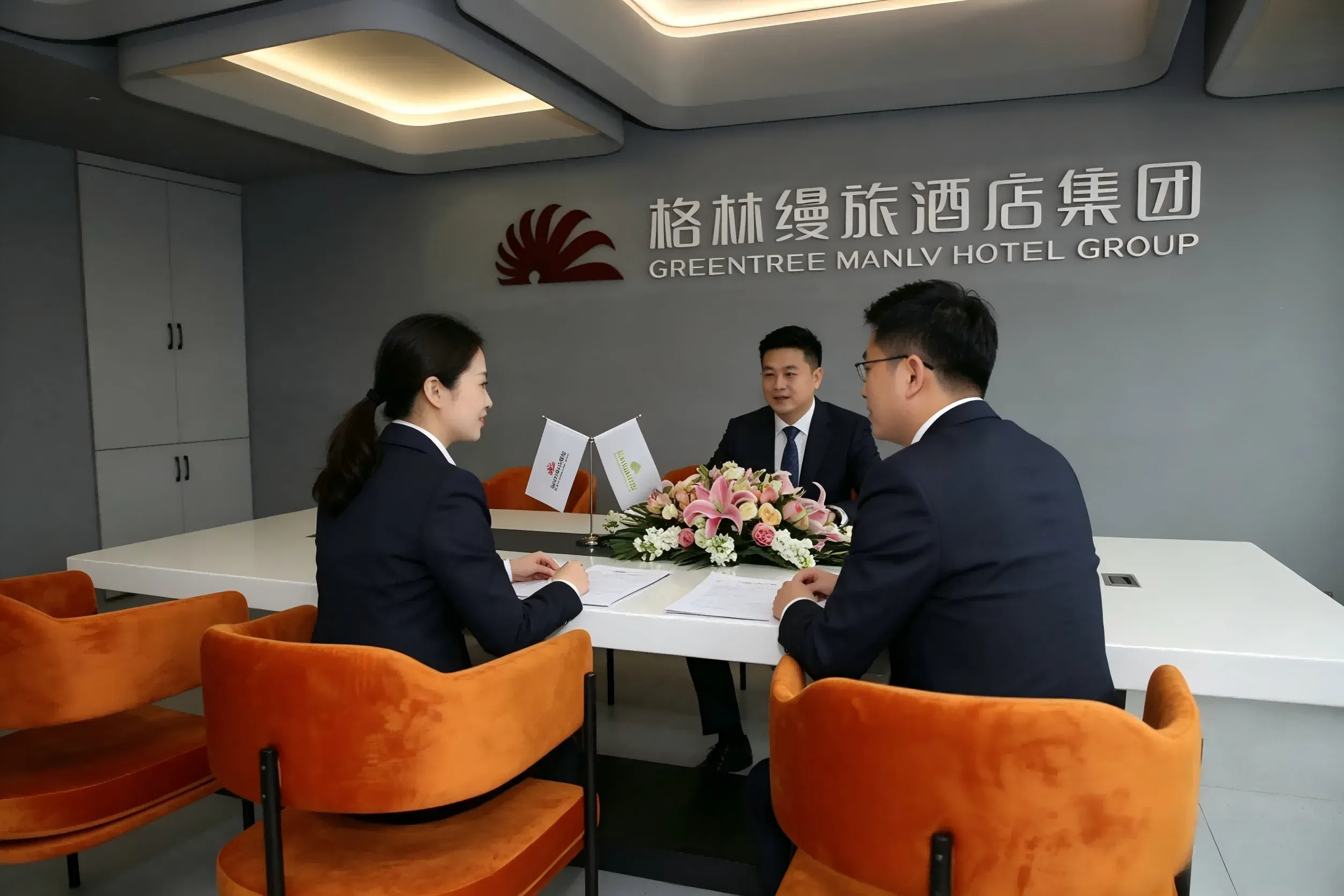 集团标志墙前三位商务人员围洽谈桌交谈，实拍，明快专业